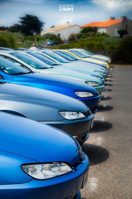 Alignement serré de Peugeot 406 Coupé bleues et jaunes vues de face sur un parking