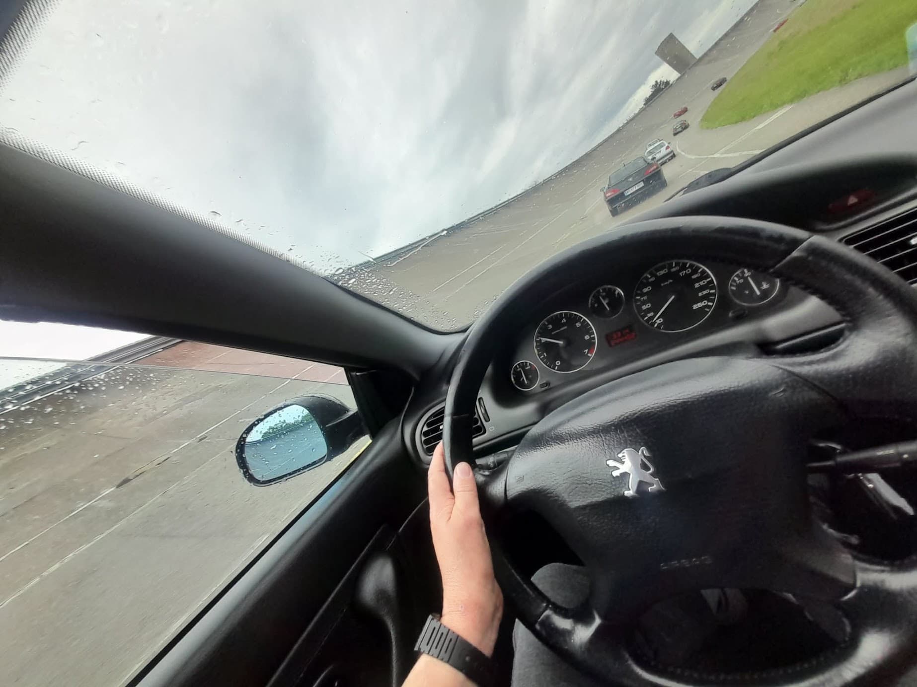 Vue depuis l'habitacle d'une 406 Coupé : volant Peugeot et compteurs, sous la pluie