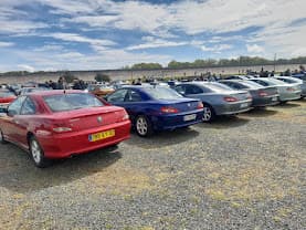 406 Coupé rouge, bleue et grises alignées sur un parking gravillonné